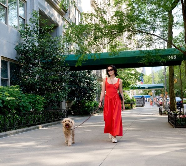 A woman in a red dress walks her dog on a sunny day in New York City