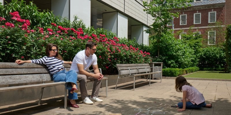 Kid drawing with chalk and parents sat on bench