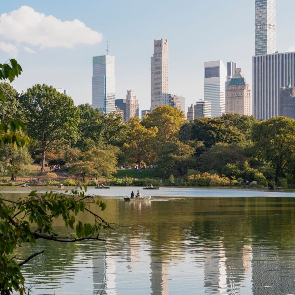 Looking across calm water in Central Park with tall buildings in the background