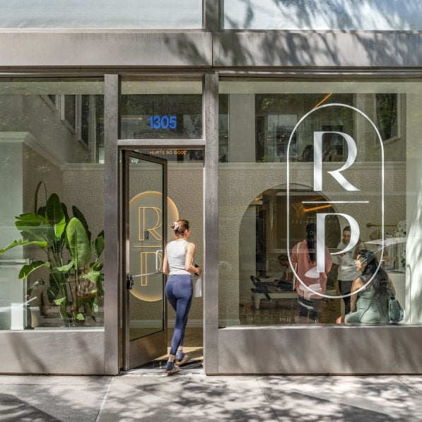 A woman in leggings opening the door to a pilates studio. 