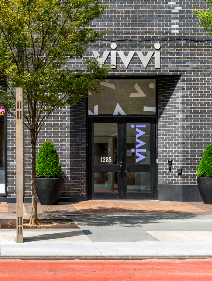 City sidewalk with small trees and store fronts, including vivvi Childcare & Early Learning 