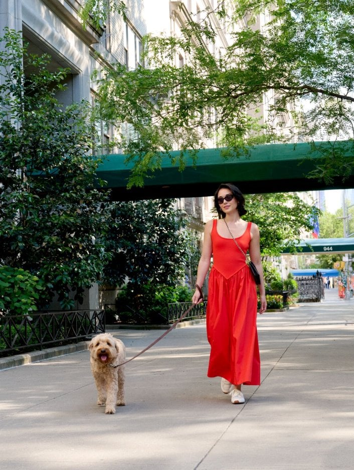 A woman in a red dress walks her dog on a sunny day in New York City