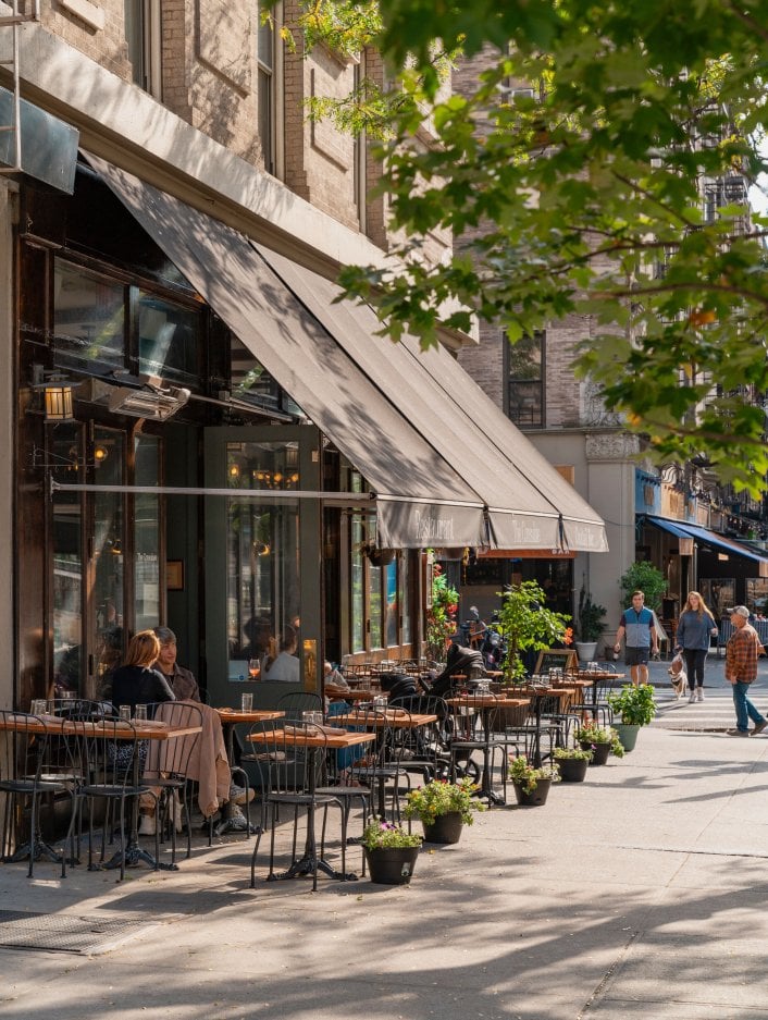 A restaurant patio on Columbus Avenue sits beside a tree on sunny day