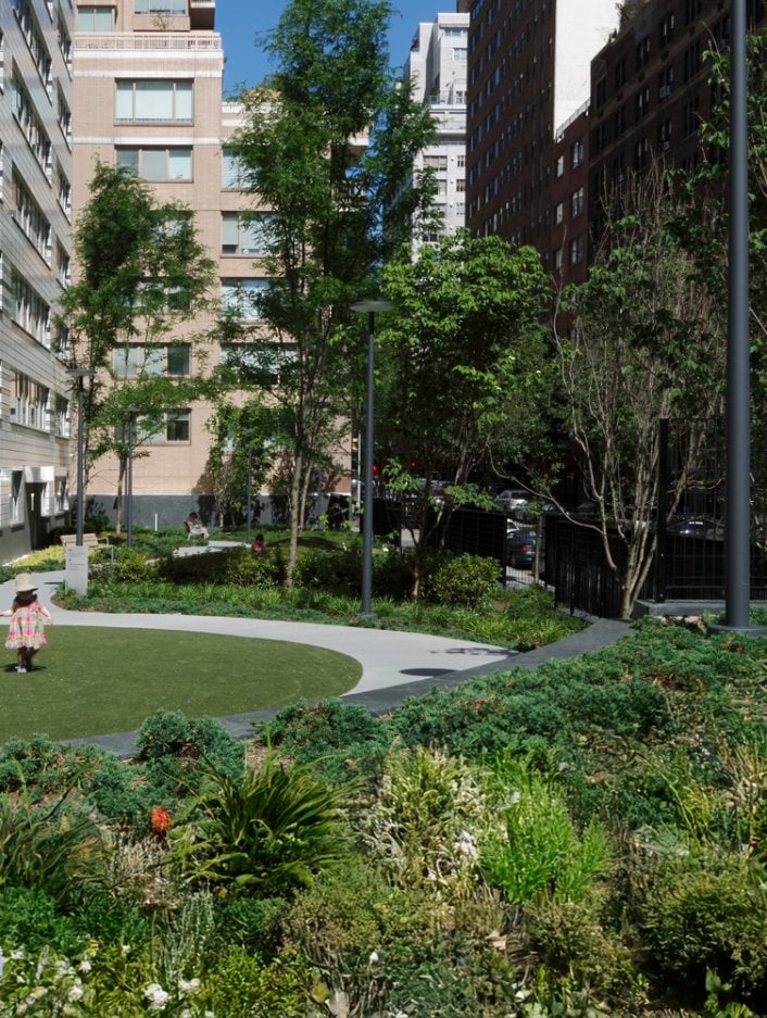 A landscaped garden with a family walking through and an apartment building in the background