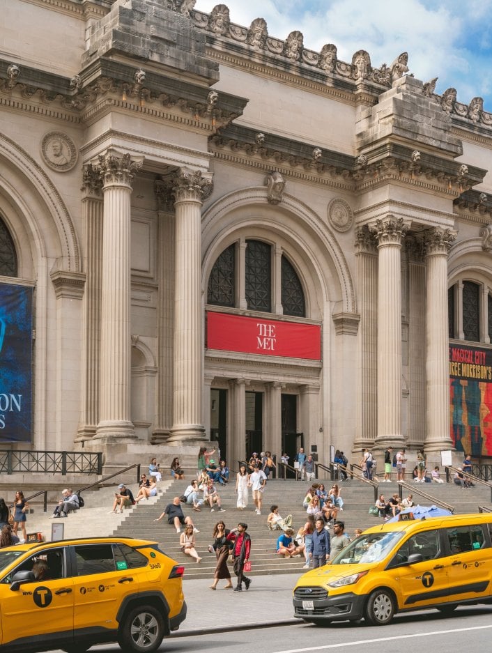 The Metropolitan Museum of Art in NYC with cars parked in front of the stairs leading to the entrance