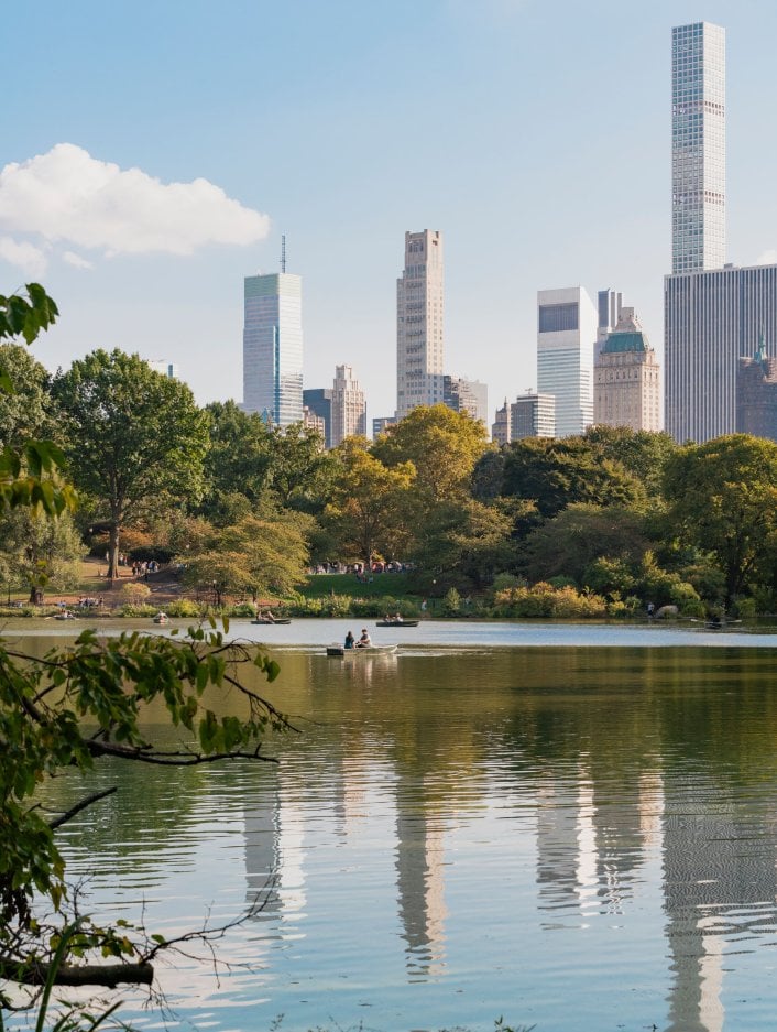 Looking across calm water in Central Park with tall buildings in the background