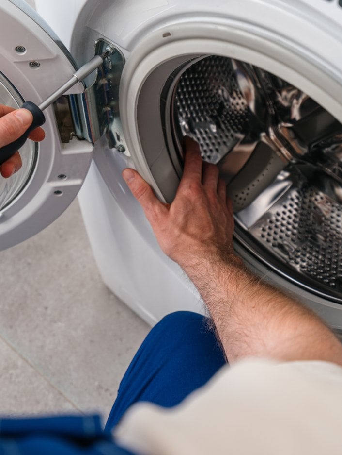 A maintenance worker tightens the door on a washing machine